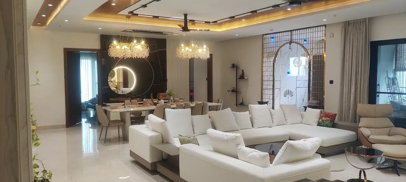 Dense open-plan room with oversized white seating, crystal chandeliers, a layered ceiling, fluted wall panels, and an ornamental metal arch
